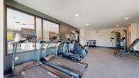 Located at 140 E Monument Ave in Dayton, Ohio, this fitness center offers a comprehensive and thoughtfully designed workout facility across a single floor. The space is divided into distinct functional zones, providing a well-rounded exercise environment for users of varying fitness levels.

The cardio area is outfitted with a row of True-brand treadmills, stair climbers, and elliptical machines, all positioned to take advantage of the facility's large floor-to-ceiling windows. These expansive windows allow abundant natural light to fill the space and offer open outdoor views, creating an energizing atmosphere during workouts.

The strength training section features a multi-function cable machine, an adjustable workout bench, and a tiered dumbbell rack stocked with a range of free weights. A wall-mounted flat-screen television is also present, adding convenience for longer training sessions.

A dedicated functional training corner is stocked with stability balls, medicine balls in various sizes, resistance bands, foam rollers, and a stair climber, catering to dynamic and mobility-focused routines.

Throughout the space, durable rubber and carpet flooring provide a safe, low-impact surface. Recessed lighting complements the natural light from the windows, maintaining a bright and clean aesthetic. The overall design uses a neutral palette with dark accent walls, lending the space a contemporary, professional feel.