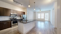 This well-appointed 2-bedroom, 2-bathroom residence is thoughtfully designed on a single floor, offering a functional and modern layout. The open-concept kitchen and living area serves as the heart of the home, featuring a central island with dark granite countertops, a stainless steel appliance suite including a gas range, microwave, and French door refrigerator, and rich dark wood cabinetry. Pendant lighting and track lighting illuminate the kitchen, while the adjoining living area benefits from large windows and a glass door that flood the space with natural light. A ceiling fan adds comfort to the bright, wood-floored living room. Both bedrooms are carpeted and generously sized, each offering direct access to a private bathroom. The spacious primary bedroom connects to an en-suite bathroom equipped with a dark wood double vanity, granite countertops, a glass-enclosed shower, and built-in shelving. Each bedroom also features dedicated closet space with wire shelving systems for organized storage. Wood-look flooring flows through the main living areas, tying together a cohesive, contemporary aesthetic throughout the residence.