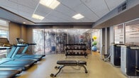 Located at 605 W Chapel Hill St in Durham, NC, this well-appointed fitness center offers a comprehensive workout environment designed to accommodate a wide range of exercise routines. The facility is organized into distinct functional zones, each tailored to specific training needs.

The main cardio area features a row of treadmills positioned along large windows that invite abundant natural light and views of the surrounding urban landscape. Alongside the treadmills, multiple elliptical machines and stair climbers round out the cardiovascular equipment offerings. Recessed and panel lighting throughout ensures consistent illumination across all areas.

A dedicated strength training section houses a variety of cable machines and resistance equipment, with open floor space and flat benches for free weight exercises. Dumbbell racks are neatly organized and accessible, supporting a full range of strength workouts.

A separate studio room features warm hardwood-style flooring, mirrored walls, and large windows that fill the space with natural light. This versatile area is equipped with a Synrgy360 functional training system and spin bikes, making it ideal for group classes or independent training sessions.

An additional functional training zone includes stability balls, kettlebells, and resistance tools stored on organized racks. The space features a suspended drop ceiling, neutral wall tones, and a clean, professional aesthetic throughout, creating an inviting and motivating environment for all fitness levels.
