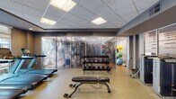 Located at 605 W Chapel Hill St in Durham, NC, this well-appointed fitness center offers a comprehensive workout environment designed to accommodate a wide range of exercise routines. The facility is organized into distinct functional zones, each tailored to specific training needs.

The main cardio area features a row of treadmills positioned along large windows that invite abundant natural light and views of the surrounding urban landscape. Alongside the treadmills, multiple elliptical machines and stair climbers round out the cardiovascular equipment offerings. Recessed and panel lighting throughout ensures consistent illumination across all areas.

A dedicated strength training section houses a variety of cable machines and resistance equipment, with open floor space and flat benches for free weight exercises. Dumbbell racks are neatly organized and accessible, supporting a full range of strength workouts.

A separate studio room features warm hardwood-style flooring, mirrored walls, and large windows that fill the space with natural light. This versatile area is equipped with a Synrgy360 functional training system and spin bikes, making it ideal for group classes or independent training sessions.

An additional functional training zone includes stability balls, kettlebells, and resistance tools stored on organized racks. The space features a suspended drop ceiling, neutral wall tones, and a clean, professional aesthetic throughout, creating an inviting and motivating environment for all fitness levels.