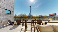 Located at 600 Calvert St in Charlotte's vibrant West End, this rooftop terrace offers a sophisticated outdoor amenity space designed for both relaxation and entertaining. The terrace is defined by its warm architectural palette, combining whitewashed brick walls with rich wood-paneled ceilings that lend a refined yet approachable character to the space.

A standout feature is the floor-to-ceiling linear fireplace set into a full-height brick surround, flanked by comfortable lounge seating — ideal for year-round use. Adjacent to the lounge area, a built-in wet bar with under-counter refrigeration and cabinet storage provides convenient amenities for hosting. Large floor-to-ceiling glass sliding doors seamlessly connect the covered terrace to the interior, flooding the transitional spaces with natural light.

The open-air section of the terrace is appointed with bar-height dining furniture and additional lounge seating, all oriented to take full advantage of the sweeping views of the Charlotte skyline. A glass balustrade ensures unobstructed sightlines across the tree-lined surroundings toward the city's downtown towers. Large-format tile paving extends throughout, unifying the covered and open-air zones into a cohesive, well-appointed rooftop retreat.