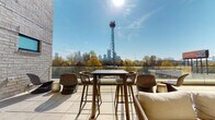 Located at 600 Calvert St in Charlotte's vibrant West End, this rooftop terrace offers a sophisticated outdoor amenity space designed for both relaxation and entertaining. The terrace is defined by its warm architectural palette, combining whitewashed brick walls with rich wood-paneled ceilings that lend a refined yet approachable character to the space.

A standout feature is the floor-to-ceiling linear fireplace set into a full-height brick surround, flanked by comfortable lounge seating — ideal for year-round use. Adjacent to the lounge area, a built-in wet bar with under-counter refrigeration and cabinet storage provides convenient amenities for hosting. Large floor-to-ceiling glass sliding doors seamlessly connect the covered terrace to the interior, flooding the transitional spaces with natural light.

The open-air section of the terrace is appointed with bar-height dining furniture and additional lounge seating, all oriented to take full advantage of the sweeping views of the Charlotte skyline. A glass balustrade ensures unobstructed sightlines across the tree-lined surroundings toward the city's downtown towers. Large-format tile paving extends throughout, unifying the covered and open-air zones into a cohesive, well-appointed rooftop retreat.