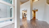 Located at 4560 Mission Gorge Pl in San Diego, CA, this two-story residence offers a thoughtfully designed interior that balances open living spaces with functional room layouts. The main level immediately impresses with its soaring double-height ceilings and an abundance of natural light streaming through tall, floor-to-ceiling windows. Structural columns frame the expansive living area, which features rich hardwood-style flooring that flows seamlessly throughout the lower level. A staircase connects the two floors, adding architectural interest to the open layout. The kitchen is well-appointed with white shaker cabinetry, dark countertops, a subway tile backsplash, and a full suite of stainless steel appliances including a gas range, microwave, refrigerator, and dishwasher. A half bathroom on the main level features marble-style tile flooring and a clean pedestal sink. Upstairs, carpeted bedrooms offer a comfortable retreat, with one room featuring an open loft-style overlook that connects visually to the lower level below. A full bathroom on the upper floor includes a light wood vanity, quartz countertop, and marble-style tile flooring. The overall aesthetic is modern and neutral, with a clean, move-in-ready feel throughout.