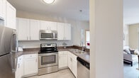 This thoughtfully designed 2-bedroom, 2-bathroom residence in Milwaukee's vibrant North Commerce Street corridor offers a functional and comfortable single-floor layout. The open-concept kitchen is a standout feature, outfitted with white shaker cabinetry, dark countertops, stainless steel appliances including a range, microwave, and refrigerator, and a breakfast bar with seating — ideal for casual dining. Adjacent to the kitchen, the dining area accommodates a bistro-style table beneath a modern chandelier, while the living room features light wood-style flooring and large sliding glass doors that open to a private balcony, flooding the space with natural light and outdoor views. Both bedrooms are carpeted and generously sized, each featuring large windows that bring in ample daylight. The spacious primary bedroom includes its own en-suite bathroom with a vanity, white cabinetry, and light-toned flooring. The second bathroom offers a full tub/shower combination with neutral finishes and a wide vanity mirror. A dedicated closet provides additional storage. The overall palette of warm neutrals and natural wood accents throughout creates a clean, welcoming ambiance well-suited for modern urban living.