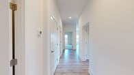 This well-designed 2-bedroom, 2-bathroom unit in Stevensville, MD offers a clean, modern aesthetic with thoughtful finishes throughout its single-floor layout. The kitchen is a standout space, featuring white shaker-style cabinetry with brushed nickel hardware, stainless steel appliances including a refrigerator, range, and over-the-range microwave, a blue-gray tile backsplash, light countertops, and a center island — all set atop light wood-style flooring that flows seamlessly through the main living areas. A bright, open living area benefits from natural light streaming through large windows, with sliding glass doors providing outdoor access and views of the surrounding landscape. The hallway connecting the rooms is clean and airy, lined with white panel doors and recessed lighting. Both bedrooms are carpeted for comfort, with the primary bedroom offering a sliding glass door and ample space. The secondary bedroom includes a double-door closet. Each bathroom is distinctly finished: one features a tiled tub-surround with a herringbone-patterned floor, while the other offers a walk-in tiled shower with large-format gray tile and matching flooring. Both bathrooms include white vanities with light countertops.