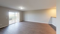 Located at 6300 E 45th St in Sioux Falls, South Dakota, this single-floor unit offers a clean, modern layout with thoughtfully selected finishes throughout. The open-concept living and kitchen area serves as the heart of the space, where durable wood-look flooring runs underfoot and neutral gray walls create a bright, versatile backdrop. A sliding glass door in the living area opens to a private balcony, allowing natural light to flow in and providing outdoor views of the surrounding landscape. The kitchen features white shaker-style cabinetry, dark countertops, recessed lighting, and black appliances, including a range and refrigerator. A peninsula counter separates the kitchen from the living space, offering additional prep and seating potential. The bedroom is carpeted for comfort, with a large window fitted with blinds that frames outdoor views and fills the room with natural light. A closet and direct access to the ensuite bathroom provide added convenience. The bathroom is appointed with a white vanity, gray stone-look countertop, a large mirror with an overhead light bar, and dark wood-look flooring. A grab bar is also present, adding accessibility to the space. Consistent neutral tones, clean lines, and practical finishes give this unit a polished, move-in-ready appeal.