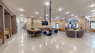 Located at 106 Stonebridge Ct in Cheshire, CT, this thoughtfully designed single-floor amenity space offers an impressive blend of recreation, fitness, and social gathering areas across a generously sized footprint.

The living room serves as the heart of the space, boasting soaring ceilings with exposed wooden beams, large glass garage-style doors that flood the interior with natural light, and a warm, inviting atmosphere. A substantial tan leather sectional, walnut coffee tables, and pendant lighting create an upscale yet comfortable lounge setting. Polished concrete floors and latticed wood-panel walls extend throughout the open social area, which also features a billiard table, dining seating, and a suspended swing chair that adds a playful architectural touch.

The exercise room is a standout, featuring vaulted ceilings with exposed wood beams, teal accent walls, and a dramatic rock-climbing mural. It is equipped with cardio machines, free weights, and a mirrored studio area with light wood flooring and a glass garage door opening to the outdoors.

The game room is equally impressive, housing a professional indoor golf simulator with green turf, a music studio corner outfitted with instruments and a vibrant speaker-themed accent wall, and additional seating for spectators. A welcoming entryway with curated wall art and a pebble-stone feature alcove completes the space.