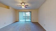 This single-floor residence is thoughtfully laid out to maximize functionality across its key living areas. The main living space is bright and open, featuring plush blue-toned carpet, a textured ceiling, and a ceiling fan with integrated lighting. A full-width sliding glass door fitted with vertical blinds opens directly onto a private balcony, allowing generous natural light to fill the room. A tiled entryway at the front door provides a practical transition point into the carpeted living area.

The galley-style kitchen is efficiently designed with warm wood cabinetry lining both sides, light-toned countertops, tile flooring, and white appliances including a range, microwave, refrigerator, and dishwasher. A utility closet is accessible directly from the kitchen.

The two bedrooms are each finished with neutral carpet and ceiling fans, and both feature windows with blinds that bring in outdoor views and natural light. One bedroom includes a walk-in closet with shelving, while the other offers a standard closet. The bathroom is finished with tile flooring, a single-sink vanity with wood cabinetry, a wall mirror, and a towel bar, maintaining a clean and functional aesthetic consistent with the rest of the space.
