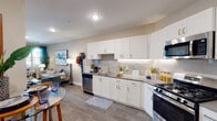 This single-floor residence offers a thoughtfully designed layout that balances comfort and functionality. The kitchen is a standout feature, outfitted with crisp white shaker cabinetry, a classic subway tile backsplash, sleek quartz countertops, and a full suite of stainless steel appliances including a gas range, built-in microwave, refrigerator, and dishwasher. Wood-look flooring runs through the kitchen and into the adjacent dining area, creating a cohesive, modern aesthetic.

The living room is bright and welcoming, with large windows dressed in teal drapes that invite natural light while providing a pop of color. A glass door leads directly to a private balcony, extending the living space outdoors. The room offers ample space for comfortable seating arrangements and entertainment.

The bedroom is a serene retreat featuring plush carpeting, a ceiling fan, and generous natural light from a window. A stylish sliding barn door opens to a spacious walk-in closet, while a separate door leads to the en-suite bathroom. The bathroom includes a full soaking tub and shower combination with clean white tile surround and warm neutral wall tones, completing the home's cohesive design palette.