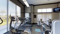 Located at 11775 Wadsworth Boulevard in Broomfield, Colorado, this fitness center offers a well-equipped, single-floor exercise facility designed to support a comprehensive workout experience. The space is thoughtfully laid out to maximize functionality and ease of movement between equipment stations.

The cardio area is a standout feature, lined with multiple treadmills and elliptical machines positioned along large windows fitted with horizontal blinds. These windows allow generous natural light to fill the space, creating an open and energizing atmosphere for users during their workouts. A full-length mirror along one wall visually expands the room and allows exercisers to monitor their form.

Complementing the cardio equipment, the strength and resistance training section is positioned along the opposite side of the room, offering a variety of machines to target different muscle groups. The flooring features patterned carpet with accent tiles in blue and gray tones, adding a modern aesthetic touch to the overall design.

Overhead fluorescent lighting ensures consistent illumination throughout the facility, while the neutral wall tones in beige and dark trim contribute to a clean, contemporary look. The layout promotes an efficient flow between equipment, making it a practical and inviting space for fitness enthusiasts of all levels.