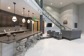 Located at 4616 Roswell Rd in Sandy Springs, GA, this striking communal lobby space makes an immediate impression with its dramatic double-height ceilings and refined contemporary aesthetic. The open floor plan is anchored by a bold contrast of polished light flooring and a dark inlaid runway strip, creating a strong visual axis throughout the space.

Floor-to-ceiling black-framed windows along the exterior wall flood the interior with natural light while offering views of the surrounding greenery. Sheer and opaque drapery panels frame these grand windows, adding texture and warmth to the otherwise sleek palette of crisp whites, deep charcoals, and rich navy accents.

A sculptural open staircase with an intricate geometric metal railing serves as a focal architectural feature, leading to an upper-level overlook balcony that reinforces the grandeur of the vertical space. The lounge area is thoughtfully appointed with contemporary upholstered seating, including plush sofas and accent chairs, arranged to encourage both social interaction and quiet relaxation.

Toward the rear, a full kitchen and bar area features dark wood cabinetry, stone countertops, stainless steel appliances, and a row of bar-height seating illuminated by a series of stylish pendant lights. Small café-style tables near the windows provide additional seating options. Glass doors at the entry provide visibility into an adjacent fitness area, completing this well-appointed amenity space.