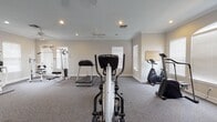 This fitness center in Ridgeland, MS offers a well-appointed, single-floor exercise facility designed to support a comprehensive workout routine. The space is finished with neutral-toned walls and wall-to-wall carpet, creating a clean and welcoming atmosphere throughout. Multiple ceiling fans and recessed lighting ensure the room remains comfortable and well-lit during any workout session. Crown molding adds a polished architectural touch along the ceiling perimeter.

The facility is equipped with an impressive selection of exercise equipment, including True-brand treadmills, an elliptical trainer, a rowing machine, a stationary upright bike, and multiple multi-function cable and strength machines. A dedicated free-weight and bench press station further rounds out the strength-training options. A water cooler station near the entrance provides easy hydration access for users.

Natural light fills the space through numerous windows fitted with white horizontal blinds, contributing to an airy and open feel. The layout provides ample floor space between machines, allowing users to move freely and safely between stations. A clearly marked entrance and exit door provides convenient access. A posted Fitness Center rules and information sign reflects the space's commitment to an organized and welcoming workout environment.