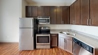 Located at 401 River St in the heart of Greenville, South Carolina, this single-floor unit offers a well-planned layout with a clean, modern aesthetic throughout. Warm hardwood-style flooring flows seamlessly across the living areas, creating a cohesive and inviting atmosphere.

The kitchen is a functional centerpiece, outfitted with rich dark espresso cabinetry reaching toward the ceiling for generous storage. Stainless steel appliances — including a refrigerator, electric range, over-the-range microwave, and dishwasher — complement the granite-style countertops and undermount sink, delivering a polished, practical cooking space.

The living area is bright and open, with neutral walls and natural light enhancing the sense of space. A ceiling fan adds to the comfort of the main room.

The bathroom is well-appointed, featuring a dark vanity with a granite-top sink and mirror, tile-surround tub/shower, and hardwood-style flooring that carries through from the rest of the unit, maintaining design consistency.

A notable convenience is the in-unit stacked washer and dryer, tucked neatly behind louvered bifold doors, providing private laundry without sacrificing space. The overall design is clean, functional, and move-in ready, making this an efficient and comfortable Greenville residence.