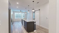 This well-appointed two-bedroom, one-bathroom unit in Northglenn, Colorado offers a thoughtfully designed single-floor layout with modern finishes throughout. The open-concept kitchen and living area serves as the heart of the home, anchored by a striking island with granite countertops and dark cabinetry, illuminated by a trio of globe pendant lights. The kitchen is equipped with stainless steel appliances, including a French door refrigerator, electric range, and built-in microwave, complemented by a tile backsplash and white upper cabinets. Light wood-look flooring flows throughout the main living areas, while a stylish barn door adds a contemporary architectural touch. The living area is bright and welcoming, benefiting from multiple windows that invite natural light, and opens to a private balcony with metal railings overlooking the landscaped community. Both bedrooms feature plush carpet, ceiling fans, and generous windows. The primary bedroom includes a walk-in closet and direct sightlines to the kitchen. The full bathroom is sleek and modern, outfitted with a granite vanity, dark cabinetry, an illuminated mirror, and a glass-enclosed shower. A dedicated laundry area and two closets round out this efficiently designed home.