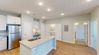 Located in Huntsville, AL, this single-floor residence offers a thoughtfully designed layout with modern finishes throughout. The kitchen serves as the centerpiece of the home, showcasing white shaker cabinetry, light granite countertops, and a full suite of stainless steel appliances including a refrigerator, range, and microwave. A generously sized central island with an integrated sink provides additional workspace and casual seating, making it ideal for both cooking and entertaining. Warm-toned hardwood-style flooring flows throughout the main living areas, complementing the soft, neutral wall tones that lend a clean and airy atmosphere. A dedicated laundry area is conveniently accessible just off the kitchen. The bedrooms offer plush carpeting, ceiling fans, and windows that invite natural light, creating comfortable and restful retreats. The bathroom features tile flooring, granite vanity counters, and a full soaking tub with a tiled surround. Recessed lighting throughout ensures well-lit spaces, while the open floor plan promotes a seamless flow between the kitchen, dining, and living areas. This residence combines practical functionality with contemporary style in a well-appointed single-level layout.