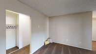 Located at 2020 W Alameda Ave in Anaheim, California, this single-floor residence offers a practical and comfortable layout with a warm, neutral aesthetic throughout. The living area is generously sized, featuring plush wall-to-wall carpeting, a ceiling fan, and a sliding glass door that opens to a private balcony, allowing natural light to flow in and providing an easy connection to the outdoors. A secondary carpeted room with a large window and vertical blinds offers flexible use as a bedroom or den. The kitchen is functionally appointed with white cabinetry, light stone-finish countertops, wood-look flooring, a coil-burner electric range, and an over-the-range microwave. The bathroom is clean and well-finished, showcasing a wide vanity with quartz-style countertops, white cabinetry, a large mirror, wood-look flooring, and a full shower/tub combo with a window above for natural ventilation. Textured ceilings are consistent throughout the unit. The overall layout, as seen in the dollhouse view, is compact yet efficiently organized, with distinct living, sleeping, cooking, and bathing zones. The space presents a move-in ready environment with a neutral palette suited to a variety of interior styles.
