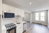 This 320 square foot studio apartment, located at 726 Franklin St in Worcester, MA, offers a thoughtfully designed living space on a single floor. The open-concept layout maximizes the available area, seamlessly blending the living room and kitchen. The living area is illuminated by large windows, providing natural light and views of the surrounding neighborhood.

The kitchen, while compact, is equipped with modern appliances including a stove and refrigerator. White cabinetry lines the walls, offering ample storage space. The bathroom features a full-sized tub-shower combination, toilet, and vanity, finished in crisp white for a clean, contemporary look.

Throughout the apartment, wood-look laminate flooring adds warmth and durability. The neutral color palette, with light gray walls and white trim, creates a bright, airy atmosphere. Recessed lighting in the ceiling provides additional illumination.

The apartment's efficient design includes built-in baseboard heating and strategically placed electrical outlets. A white entry door leads into the space, and a fire alarm system ensures safety. This studio apartment offers a comfortable, low-maintenance living option in an urban setting.