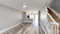 This three-floor home in Columbus, Ohio offers a thoughtfully designed layout spread across well-proportioned levels. The ground floor features a combined kitchen and living area, where a sleek, modern kitchen takes center stage with gray shaker-style cabinetry, a bold mosaic tile backsplash, white quartz countertops, stainless steel appliances, a built-in cooktop, and a striking stainless steel island range hood. Pendant lighting and large windows fill the space with natural light, complementing the durable wood-look flooring found throughout the main and lower levels. The lower level includes a spacious living room with painted cinder block walls, a full bathroom with a pedestal sink, and a dedicated laundry room equipped with a full-size washer and dryer. A utility room rounds out this floor. The upper level houses two bedrooms, including a generously sized primary bedroom with soft carpeting, neutral gray walls, and a double sliding closet. The second bedroom mirrors this clean, comfortable aesthetic. A full bathroom with a shower-tub combo and wood-look flooring serves the upper level. Staircases connect all three floors efficiently, and a hallway ties the upper level together for a functional, cohesive flow throughout the home.