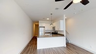 Located at Greenview Towns in Bay Shore, New York, this two-floor townhome offers a thoughtfully designed layout with modern finishes throughout. The main level features an open-concept living and kitchen area anchored by warm hardwood-style flooring. The kitchen is well-appointed with crisp white shaker cabinetry, dark countertops, a stainless steel appliance suite including a gas range, built-in microwave, refrigerator, and dishwasher, along with a peninsula that provides additional prep space and an integrated sink. Pendant lighting and a ceiling fan add both function and style to the living area, while natural light flows in through multiple windows. A convenient half bathroom with a white vanity and oval mirror is also found on this level. The upper floor hosts bedrooms, including a room with vaulted ceiling details and plush carpeting, as well as a full bathroom featuring a white vanity, tub-shower combination, and wood-style flooring. A dedicated in-unit laundry area with a full-size washer and dryer completes the home. Clean, neutral tones and contemporary hardware are consistent throughout, creating a bright and inviting living environment.