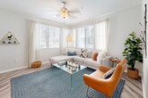 This single-story home offers a thoughtfully designed layout across a comfortable footprint, featuring four bedrooms, two bathrooms, a living room, dining area, and kitchen. The interior is finished with a contemporary palette of soft grey walls, light wood-style flooring in the main living areas, and plush carpet in the bedrooms, creating a cohesive and inviting atmosphere throughout.

The kitchen is a standout space, featuring dark cabinetry contrasted by light quartz countertops, stainless steel appliances including a full refrigerator, range, microwave, and dishwasher, and a window at the end that draws in natural light. The adjacent dining area benefits from wood-look flooring, decorative wall shelving, and ample natural light from a sliding door. The living room is well-proportioned with large windows providing outdoor views and a warm, modern ambiance.

The primary bedroom is generously sized with a large window, soft carpet, and neutral tones. Additional bedrooms share similar finishes. Both bathrooms are clean and modern, each featuring dark wood vanities with white countertops, large mirrors, wood-look flooring, and shower-tub combinations with curtains.