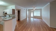 This single-floor residence offers a thoughtfully designed layout that balances comfort and functionality throughout. The open-concept living and dining area is a standout feature, showcasing warm hardwood flooring that extends seamlessly across the space. Large windows and a front entry door flood the area with natural light, while a ceiling fan adds both style and practicality. Track lighting near the entry provides additional illumination, and crown molding adds a refined architectural touch.

The kitchen is well-equipped, featuring granite-style countertops, ample cabinetry, and a full suite of white appliances including a refrigerator, range, dishwasher, and microwave. A breakfast bar separates the kitchen from the living space, offering a convenient casual dining option. Adjacent to the kitchen, a dedicated laundry area houses a full-sized washer and dryer alongside shelving and an electrical panel access point.

The carpeted bedroom is a comfortable retreat, complete with a ceiling fan and a window offering views of lush greenery. A generously sized walk-in closet fitted with wire shelving and hanging rods provides ample storage. The full bathroom includes a tiled tub-and-shower combo, a single vanity with extended countertop and cabinetry, and tile flooring, rounding out this move-in-ready residence.