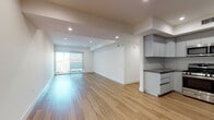 This single-floor unit showcases a clean, contemporary design characterized by warm light wood flooring, crisp white walls, and recessed lighting throughout. The open-concept living and dining area is generously proportioned, offering a seamless flow enhanced by a sliding glass door that leads to an outdoor space, drawing in natural light and providing outdoor views.

The kitchen is efficiently designed with flat-front gray cabinetry, dark countertops, a white subway tile backsplash, and a full suite of stainless steel appliances, including a French door refrigerator, gas range, microwave, and dishwasher. A built-in cabinetry nook with additional counter space extends the kitchen's functionality into the living area.

The bedrooms feature the same light wood flooring with clean white walls; one bedroom includes a large window with outdoor views and benefits from abundant natural light. The bathrooms are finished with large-format gray tile, glass-enclosed walk-in showers equipped with both fixed and handheld showerheads, and modern vanities with undermount sinks and taupe countertops. Throughout, the space maintains a consistent, minimalist aesthetic with cohesive finishes.
