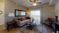 This single-floor residence offers a thoughtfully designed layout that balances comfort and functionality across its key living areas. The living room serves as the heart of the home, featuring wood-style flooring, a ceiling fan with light fixture, and a large sliding glass door that opens onto a private balcony, flooding the space with natural light and providing open outdoor views. A sizeable wall mirror enhances the sense of space, while textured curtains add warmth to the room's overall ambiance. The kitchen is efficiently laid out with rich dark cabinetry, light countertops, and a full suite of appliances including a gas range, built-in microwave, and stainless steel refrigerator. Adjacent to the living area, the dining space accommodates a full six-seat table and features a framed pass-through window that connects visually to the kitchen, along with warm artwork that adds character to the room. The bedroom is a serene retreat with plush carpeting, a large window with natural light, and ample room for a dresser and seating area. The bathroom continues the home's cohesive design with dark wood cabinetry, wood-style flooring, and clean, neutral walls. Together, these spaces create a well-rounded, inviting home environment.