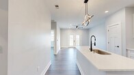 Located in South Lebanon, Ohio, this thoughtfully designed single-floor residence offers a generous, open-concept layout that balances modern aesthetics with everyday functionality. The combined kitchen and living area serves as the heart of the home, anchored by a large quartz-topped island with an undermount sink and a striking sculptural pendant light. White shaker cabinetry lines the kitchen walls alongside stainless steel appliances, including a range, over-the-range microwave, and a French-door refrigerator. A dedicated pantry provides additional storage. Warm wood-look flooring flows throughout the entire space, complementing the soft gray walls and crisp white trim. The living room is bright and spacious, featuring recessed lighting, a ceiling fan, and French doors that open onto a private balcony. From the balcony, expansive views of rolling green fields and open Ohio countryside create a serene outdoor retreat. The bedroom is well-proportioned, benefiting from its own ceiling fan and direct access to a walk-in closet. The full bathroom is finished with a white shaker vanity, quartz countertop, matte black hardware, and a tub-shower combination. A utility room and additional closet space round out this clean, move-in-ready residence.