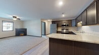 This single-floor residence offers a thoughtfully designed open-concept layout that seamlessly connects the kitchen and living areas. The kitchen is a standout feature, outfitted with dark espresso-toned shaker-style cabinetry, light granite-style countertops, and a full suite of stainless steel appliances including a refrigerator, range, microwave, and dishwasher. A peninsula counter extends into the living space, providing additional prep and seating space while maintaining an open flow throughout.

The living area transitions from light wood-look luxury vinyl plank flooring to plush carpeting, offering warmth and comfort underfoot. A corner fireplace adds a cozy focal point to the space, while a ceiling fan circulates air efficiently. Natural light filters in through windows, lending brightness to the interior.

A hallway connects the private areas of the unit, where dark craftsman-style doors add a refined touch. In-unit stacked washer and dryer are conveniently tucked into the hallway. The bathroom features a full tub-shower combination, a dark-cabineted vanity with a light countertop, and light wood-look flooring. Bedrooms are carpeted and include ceiling fans and windows with neighborhood views.