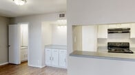 Located at 2201 Rocky Lane in Odessa, Texas, this two-story space offers a straightforward, functional layout with a light and neutral design throughout. The kitchen is a standout area, featuring white cabinetry with brushed nickel hardware, granite-look countertops, and a black range with overhead ventilation. A pass-through window connects the kitchen to an adjacent area, enhancing the open feel between spaces. A separate built-in cabinetry nook with its own countertop and overhead bar lighting provides additional workspace or storage. Wood-look flooring runs through the main living and kitchen areas, adding warmth to the otherwise bright, white interior. The bathroom includes a full tub and shower combination with built-in corner shelving and clean white tile surround, complemented by chrome fixtures. A generously sized walk-in closet features multiple shelving tiers and hanging rods, offering ample storage. The carpeted bedroom connects directly to the bathroom and closet, creating a practical private suite. Textured walls and ceilings are consistent throughout, contributing to the space's classic residential character.