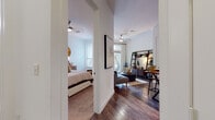 This well-appointed single-floor residence offers a thoughtfully designed layout that seamlessly connects its living spaces. Rich hardwood flooring flows throughout the main areas, complementing the clean white walls and creating a warm, modern aesthetic.

The open living area is bright and inviting, centered around a ceiling fan and filled with natural light from large sliding glass doors that lead to a private balcony — perfect for relaxing or enjoying outdoor views. The space comfortably accommodates a generous seating arrangement alongside a dedicated workspace or dining nook.

The kitchen is a standout feature, showcasing bold dark cabinetry that extends to the ceiling, granite countertops, a classic tile backsplash with under-cabinet lighting, and a full suite of stainless steel appliances. A butcher block dining table provides a natural gathering spot adjacent to the kitchen.

The bedroom is a calm retreat, carpeted for comfort and filled with soft natural light from windows on multiple walls. It connects conveniently to the kitchen area, making the overall floor plan feel cohesive.

The bathroom is finished with the same dark cabinetry and granite countertops seen in the kitchen, paired with hardwood-style flooring and a large vanity mirror. A walk-in closet is accessible directly from the bathroom, adding practical storage and enhancing the sense of a private suite.