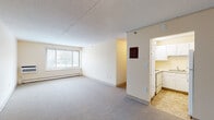 Located at 109 Broad St in Weymouth, Massachusetts, this single-floor unit offers a functional and well-organized layout designed for comfortable living. The generously sized living area is finished with neutral-toned carpet and features large windows that allow ample natural light to fill the space, along with baseboard heating throughout. The room flows seamlessly toward a separate kitchen, which is equipped with white cabinetry, laminate countertops, a stainless steel sink, and tile flooring, providing a clean and practical workspace. The bedroom is a well-proportioned room with carpeted flooring, a large window overlooking the surrounding greenery, and a built-in closet with bifold doors offering convenient storage. An additional carpeted room provides flexible space that could serve various purposes. The full bathroom is appointed with tile flooring, a combined tub and shower unit, a wood-toned vanity, and multiple grab bars, reflecting a thoughtfully accessible design. Neutral warm tones are carried throughout the unit, contributing to a cohesive and inviting atmosphere. A fire safety alert device is also present, underscoring the unit's attention to resident safety. The overall layout is practical, bright, and well-suited for everyday living.