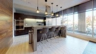 Located at 116 W 9th St in Wilmington, Delaware, this single-floor commercial space offers a sleek, contemporary design with a cohesive blend of materials and finishes throughout. Floor-to-ceiling windows line the exterior walls, flooding the interior with abundant natural light and providing open views of the surrounding streetscape.

The kitchen is a standout feature, designed with dark cabinetry, stainless steel appliances, a mosaic tile backsplash, and light-toned large-format tile flooring. A substantial central island with a concrete-style countertop and modern bar seating serves as both a functional workspace and a social gathering point, complemented by decorative pendant lighting overhead.

The open lounge and dining areas feature wood-look tile flooring and are furnished with contemporary seating, including distinctive yellow accent chairs that add a pop of color against the neutral palette. A patterned houndstooth-style feature wall adds visual texture to the seating zones, while warm wood wall panels provide an additional layer of refinement.

Glass-partitioned corridors and interior rooms allow sightlines to flow freely across the space, enhancing the sense of openness. A dedicated lounge nook with modern swivel chairs and a small side table offers a more intimate setting. Throughout, the design balances professional functionality with inviting communal spaces, making this a well-appointed and versatile commercial environment.