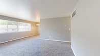 Located on Purdue Avenue in Baltimore, MD, this one-bedroom, one-bathroom single-floor unit offers a practical and well-organized layout. The combined living and dining area is an open, carpeted space finished with neutral gray walls and clean white trim. A chandelier anchors the dining portion of the room, while a large window allows natural light to fill the space and provides outdoor views of the surrounding neighborhood. The kitchen features warm wood-toned cabinetry paired with white appliances, offering a functional workspace. The bedroom is a generously sized, carpeted retreat with large windows that invite natural light and outdoor views. It is served by two closets — one a built-in with shelving and hanging rods behind bifold doors, and another open shelving closet — providing ample storage. The full bathroom features tile flooring in earthy tones, a full-size tub and shower combination with white subway tile surround, and a wood-toned vanity. Consistent gray carpeting, neutral wall tones, and white accents throughout the unit create a cohesive, clean aesthetic. Central HVAC vents are present in multiple rooms, ensuring year-round comfort. The overall layout is efficient and well-suited for single occupancy or a couple.