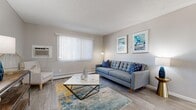 This thoughtfully designed 2-bedroom, 1-bathroom unit offers a practical and comfortable single-floor layout encompassing six distinct spaces: a living room, dining room, kitchen, two bedrooms, and a full bathroom connected by a hallway.

The living room is a bright and welcoming space, featuring large windows with vertical blinds that allow generous natural light to fill the room. Wood-look flooring, a textured ceiling, and a wall-mounted air conditioning unit complete the space.

Adjacent to the living room, the dining area provides a cozy setting with the same flooring and easy access to the kitchen. The kitchen is well-equipped with crisp white shaker cabinetry, light countertops, and a full suite of stainless steel appliances including a range, over-the-range microwave, refrigerator, and dishwasher, all set on durable wood-look flooring.

Both bedrooms feature plush carpeting, ceiling fans, windows with sheer curtains for natural light, and full-width mirrored sliding closet doors that enhance the sense of space. The primary bedroom offers a comfortable, restful retreat.

The bathroom includes a combined tub and shower with wood-look tile flooring. Throughout the unit, a neutral warm-grey palette creates a cohesive and inviting ambiance.