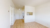 Located at 3055 N Flowing Wells Rd in Tucson, Arizona, this efficient one-bedroom, one-bathroom unit offers a practical and well-organized layout across a single floor. The galley-style kitchen is thoughtfully designed with white cabinetry featuring brushed nickel hardware, granite-look countertops, a double-basin sink, a coil-burner electric range, and a full-size refrigerator, all set atop warm beige tile flooring that continues into the adjacent living and dining area. The living space is bright and open, with a ceiling fan overhead, a wall-mounted HVAC vent, and neutral white walls that lend a clean, airy feel throughout. The bedroom is a cozy, carpeted retreat with soft neutral tones, white walls, and a window fitted with horizontal blinds that allow for natural light and outdoor views. The bathroom includes a full soaking tub and shower combo with classic white subway tile surround and chrome fixtures, alongside a toilet and vanity. A dedicated utility area houses the water heater, providing practical functionality within the unit's compact footprint. This unit offers a straightforward, move-in-ready layout well-suited for those seeking a manageable, low-maintenance living space in Tucson.