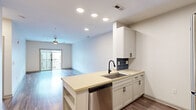 Located at 900 E Six Forks Rd in Raleigh, NC, this two-bedroom, one-bathroom unit offers a thoughtfully designed single-floor layout. The open-concept living and kitchen area serves as the heart of the home, featuring durable wood-style flooring, recessed lighting, and a ceiling fan. The kitchen is well-appointed with white shaker cabinetry accented by matte black hardware, light quartz countertops, a blue tile backsplash, a stainless steel undermount sink with a black pull-down faucet, and stainless steel appliances including a refrigerator, range, microwave, and dishwasher. A peninsula provides additional prep space and a natural division between the kitchen and living area, which opens to a private balcony. The bedrooms offer plush carpeting and ceiling fans, with the primary bedroom featuring a generous walk-in closet with wire shelving. The bathroom includes a full soaking tub with a tiled shower surround and built-in shelving. A dedicated laundry room with overhead cabinetry accommodates a full-size washer and dryer. The clean, neutral palette throughout creates a bright and functional living environment.