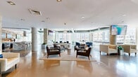 Located at 500 West Ave in Norwalk, Connecticut, this single-floor amenity lounge offers a generously proportioned open-concept space that blends industrial and contemporary design with striking effect. Polished concrete floors extend throughout, reflecting natural light that pours in through floor-to-ceiling windows lining the perimeter and framing views of the surrounding Norwalk streetscape.

The space is defined by rich textural contrasts: reclaimed wood-paneled walls warm the kitchen area, while stacked stone accent walls anchor the entrance and lounge zones, adding rustic character to the otherwise sleek interior. Exposed ductwork and concrete ceilings in select areas reinforce the industrial aesthetic, complemented by structural columns that punctuate the floor plan without interrupting the open flow.

A central kitchen bar with a marble-topped island and row of modern stools serves as a social hub, ideal for gatherings. Multiple distinct seating clusters — featuring upholstered armchairs, low-profile coffee tables, and area rugs — create flexible lounge environments suited to both quiet relaxation and group socializing. Mounted flat-screen displays are positioned throughout for shared viewing. A shuffleboard table adds a recreational focal point. The overall ambiance is welcoming, modern, and thoughtfully curated for community use.