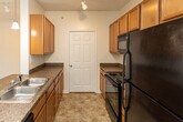 Located at 1185 W Mountain View Rd in Johnson City, Tennessee, this single-floor unit offers a well-designed, functional layout with comfortable living spaces throughout. The kitchen serves as a central feature, showcasing warm honey-toned cabinetry, dark granite-style countertops, and a suite of black appliances including a gas range, refrigerator, and microwave. A peninsula with a double sink and pendant lighting overhead creates a natural divide between the kitchen and the open living area, while track lighting adds additional illumination. A dedicated pantry closet adjacent to the kitchen provides generous storage space. The living area is open and airy, featuring plush carpeting, crown molding, ceiling fan, and track lighting. French doors lead to an outdoor access point, inviting natural light into the room. A secondary bedroom offers comfortable proportions, plush carpet, a ceiling fan, and a window with views of the surrounding neighborhood. The bathroom is cleanly finished with white tile surround enclosing a deep soaking tub and shower combination, complemented by built-in shelving and wire closet organizers nearby. Tile flooring runs throughout the kitchen and entry areas, while soft carpet covers the living and bedroom spaces, creating a warm and inviting atmosphere throughout this well-appointed Johnson City residence.
