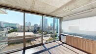 Located at 707 10th Ave in San Diego's vibrant downtown corridor, this modern urban residence showcases an industrial-contemporary design defined by exposed concrete ceilings and sleek wood-style flooring throughout. The open living and kitchen area is dominated by expansive floor-to-ceiling sliding glass windows that frame panoramic views of the San Diego skyline, flooding the space with abundant natural light and creating a strong visual connection to the city below.

The kitchen is well-appointed with granite countertops, warm wood cabinetry, white upper cabinets, stainless steel appliances including a range, microwave, and dishwasher, and a double-basin sink. A hallway leads to the private areas of the unit, where a stacked washer and dryer are conveniently housed behind louvered closet doors. The bedroom features an exposed concrete ceiling, a spacious sliding-door closet, and direct access to the bathroom. The bathroom includes a granite-topped vanity with wood cabinetry, a large mirror, and a combination shower/bathtub. Consistent wood-style flooring runs throughout, tying together the industrial and modern elements for a cohesive, contemporary aesthetic well-suited to urban living.