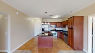 This single-floor residence is thoughtfully designed with a functional and cohesive layout. The kitchen serves as a central highlight, showcasing rich cherry wood cabinetry with dark granite countertops, a curved center island illuminated by a pendant light fixture, and a full suite of stainless steel appliances including a French door refrigerator, gas range, built-in microwave, and dishwasher. Tile flooring runs throughout the kitchen and extends toward the entry areas.

The open-concept design connects the kitchen seamlessly to a generously sized living area finished with neutral-toned carpet. Multiple windows and sliding glass door access to a balcony allow for abundant natural light throughout this space. The primary bathroom features a corner soaking tub, a separate glass-enclosed shower, a dark granite vanity with cherry cabinetry, and tile flooring. A secondary bathroom offers a standalone glass shower, toilet, and matching tile floors. Bedrooms are carpeted and include mirrored sliding closet doors. An in-unit laundry closet accommodates a full-size side-by-side washer and dryer.