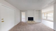 This single-floor residence offers a well-organized layout with a neutral, light-toned palette throughout. The living room serves as the heart of the space, centered around a classic brick-hearth fireplace flanked by built-in white shelving — ideal for storage or display. Plush carpet underfoot and a textured ceiling add warmth to the room, which connects seamlessly to an adjacent area with hardwood-style flooring and access to an outdoor balcony.

The galley-style kitchen is efficiently designed with white cabinetry, dark granite-style countertops, a double-basin sink, and white appliances including a range and refrigerator. Light wood-style flooring and overhead lighting keep the space bright and functional.

The bedrooms are carpeted and generously sized, each benefiting from large windows that draw in natural light and offer views of surrounding greenery. The rooms provide a calm, comfortable retreat with clean white walls and ample space for furnishings.

The bathroom features a practical layout with a vanity topped with dark granite counters, white cabinetry, wood-style flooring, and a separate water closet. Throughout the residence, the consistent use of white trim, neutral tones, and natural light creates a cohesive and inviting atmosphere.