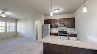 Located in Cottleville, Missouri, this single-floor, 2-bedroom, 2-bathroom residence offers a well-designed layout with functional and attractive finishes throughout. The kitchen serves as a central focal point, featuring rich dark-stained cabinetry, a white subway tile backsplash, stainless steel appliances — including a refrigerator, range, and built-in microwave — and a granite-topped island with a double basin sink and pendant lighting overhead. The layout opens toward the carpeted living area, which benefits from multiple windows and a ceiling fan, filling the space with natural light and views of the outdoors. A glass-panel door provides additional access to the exterior. The primary bedroom is a comfortable, well-proportioned retreat with plush carpet, a ceiling fan, and a dedicated closet featuring built-in shelving for ample storage. The second bedroom is equally bright, with soft carpet and natural light. Both bathrooms are finished with dark wood vanities, white countertops, and wood-look vinyl plank flooring. One bathroom features a tub-shower combination with a curved chrome curtain rod. Neutral wall tones and consistent design choices throughout create a cohesive, move-in ready atmosphere.