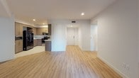 This single-floor unit presents a clean, modern aesthetic defined by neutral tones and quality finishes. The kitchen serves as a functional centerpiece, outfitted with flat-front cabinetry in a warm wood-grain finish, speckled granite countertops, stainless steel appliances including a gas range and dishwasher, and a large side-by-side refrigerator. A stainless undermount sink with a contemporary gooseneck faucet completes the well-organized workspace.

The open living area flows naturally from the kitchen, featuring light wood-look plank flooring, recessed lighting, and crisp white walls that contribute to a bright, airy atmosphere. The layout connects seamlessly to a hallway leading to additional rooms. Bedrooms are finished with soft wall-to-wall carpeting and white walls, offering a quiet and comfortable retreat. Electrical outlets are thoughtfully placed throughout.

The bathroom features a wood-toned vanity with a white countertop, an undermount sink, brushed nickel hardware, and a large mirror with integrated lighting above. Clean white walls and tile flooring reinforce the unit's cohesive modern design. Overall, the space presents a practical and polished environment suited for everyday living.