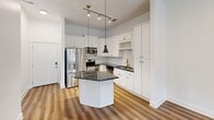 Located at Lakeside Lofts in Cary, NC, this thoughtfully designed one-bedroom, one-bathroom residence offers a clean, modern aesthetic throughout. Warm wood-tone flooring flows consistently across the open-plan layout, complementing the crisp white walls and abundant natural light that streams in through multiple windows and glass French doors.

The combined kitchen and living area serves as the heart of the home. The kitchen is well-equipped with white shaker-style cabinetry, dark granite countertops, a central island, stainless steel appliances including a refrigerator with ice maker, range, and microwave, along with stylish pendant lighting and a wine rack built into the upper cabinetry. The adjoining living area opens to the outdoors via French doors, extending the sense of space.

The bedroom is generously proportioned, featuring a ceiling fan, large windows that invite natural light and outdoor views, and a double-door closet providing ample storage. The bathroom is finished with tile flooring, a dark granite vanity countertop, framed mirror, and a glass-enclosed walk-in shower. A dedicated laundry room with full-size washer and dryer units and overhead shelving adds everyday convenience. This unit combines functional design with contemporary finishes throughout.