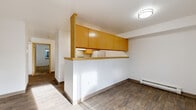 Located at 3115 Racine St in Bellingham, WA, this two-bedroom, one-bathroom unit offers a practical and well-organized single-floor layout. Wood-look plank flooring runs throughout the main living areas, lending warmth and consistency to the space.

The living room is bright and open, benefiting from a large window that frames a view of lush greenery outside, complemented by a baseboard heating unit beneath it. It flows naturally toward the kitchen, which is separated by a half-wall peninsula topped with warm honey-toned upper cabinetry — a functional design that maintains an open connection between the two spaces. The kitchen itself is galley-style, featuring ample light wood cabinetry on both upper and lower levels, a stainless steel sink, light countertops, and a full suite of white appliances including a refrigerator, range, and dishwasher.

A central hallway connects the bedrooms and bathroom, with light wood-trimmed doors and a clean, neutral color palette throughout. Both bedrooms are carpeted and feature sliding-door closets with built-in hanging rods. The primary bedroom offers a comfortable footprint well-suited for a standard bedroom arrangement. The bathroom includes a full tub-shower combo with chrome fixtures and clean white surround. Baseboard heaters are present in multiple rooms, ensuring consistent climate control.