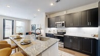 This single-floor residence offers a thoughtfully designed open-concept layout that seamlessly connects the kitchen, dining, and living areas. The kitchen is a standout feature, showcasing dark shaker-style cabinetry, granite countertops, a subway tile backsplash, and a full suite of stainless steel appliances including a refrigerator, range, and microwave. A large kitchen island with an undermount sink provides generous prep space and serves as a natural gathering point. Light wood-style flooring runs throughout, adding warmth and continuity to the space. The living area is bright and welcoming, benefiting from multiple windows that invite natural light and offer views to the outside. The entry foyer is defined by a glass-panel front door flanked by a window, creating an airy and open first impression. The bedroom is comfortably proportioned, featuring a ceiling fan, a window with natural views, and wood-style flooring. The bathroom maintains the same design language as the rest of the home, with dark cabinetry, granite countertops, an undermount sink, a large mirror, and a shower-tub combination. Clean lines, neutral tones, and consistent finishes give the entire space a cohesive, modern aesthetic.
