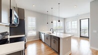 Located at Grandview Crossing in Columbus, OH, this 2-bedroom, 2-bathroom residence offers a thoughtfully designed single-level layout with modern finishes throughout. The open-concept kitchen and living area serves as the heart of the home, featuring warm hardwood flooring, a large central island with white quartz countertops and an undermount sink with a matte black faucet. Pendant lighting illuminates the space, while stainless steel appliances — including a French door refrigerator, electric range, and built-in microwave — complement the sleek gray cabinetry and white subway tile backsplash. Multiple windows flood the living and kitchen areas with abundant natural light. The two bedrooms are finished with plush carpeting and bright windows offering outdoor views. The primary bedroom includes a dedicated closet with built-in shelving and hanging rods for organized storage. The bathroom is cleanly appointed with a white quartz vanity, matte black fixtures, a bold navy-framed mirror, and a tub-shower combination. A second living space with hardwood flooring and a built-in ledge adds versatile functionality. Neutral gray walls and clean white trim create a cohesive, contemporary aesthetic throughout the entire residence.
