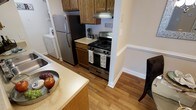 This single-floor residence offers a thoughtfully designed living space with a focus on functionality and comfort. The kitchen serves as a central highlight, featuring stainless steel appliances including a gas range and a full-size refrigerator. Warm-toned wood cabinetry provides ample storage, while light-colored countertops offer generous prep space. A kitchen peninsula adds additional workspace and subtly defines the kitchen's boundary from the adjacent dining area. Hardwood-style flooring runs throughout the space, lending a cohesive and inviting aesthetic. The kitchen also accommodates in-unit laundry, adding a layer of everyday convenience. Neutral wall tones and clean white baseboards contribute to a bright, clean atmosphere. The open sightlines between the kitchen and dining area create a connected, easy-flowing layout that is both practical and welcoming. Overall, the space combines classic finishes with modern stainless steel appliances to create a comfortable and well-equipped home environment.