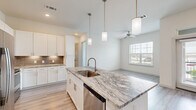 Located at 9779 Fannin Railway in Houston, TX, this single-story unit offers a thoughtfully designed layout across a compact yet functional floor plan. The open-concept kitchen and living area serves as the heart of the space, featuring light wood-look flooring that enhances the bright, airy atmosphere throughout. The kitchen is well-equipped with white shaker-style cabinetry reaching toward the ceiling, granite countertops, a large island with pendant lighting, stainless steel appliances, and a taupe tile backsplash that adds a warm contrast to the white cabinetry.

The living area flows seamlessly from the kitchen, benefiting from natural light admitted through large windows with horizontal blinds. Ceiling fans are present in multiple rooms, contributing to both comfort and airflow.

The bedroom features plush carpeting, a ceiling fan, and a wide window that allows natural light to fill the room. A dedicated closet provides additional storage. The two bathrooms are finished with granite-topped vanities, white cabinetry, wood-look flooring, and tiled tub-shower combinations, offering a clean and consistent aesthetic. Overall, the unit presents a modern, neutral palette suitable for a range of interior styles.